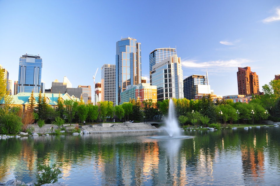 Calgary skyline at dusk with the Rocky Mountains visible on the horizon and the Bow River in the foreground