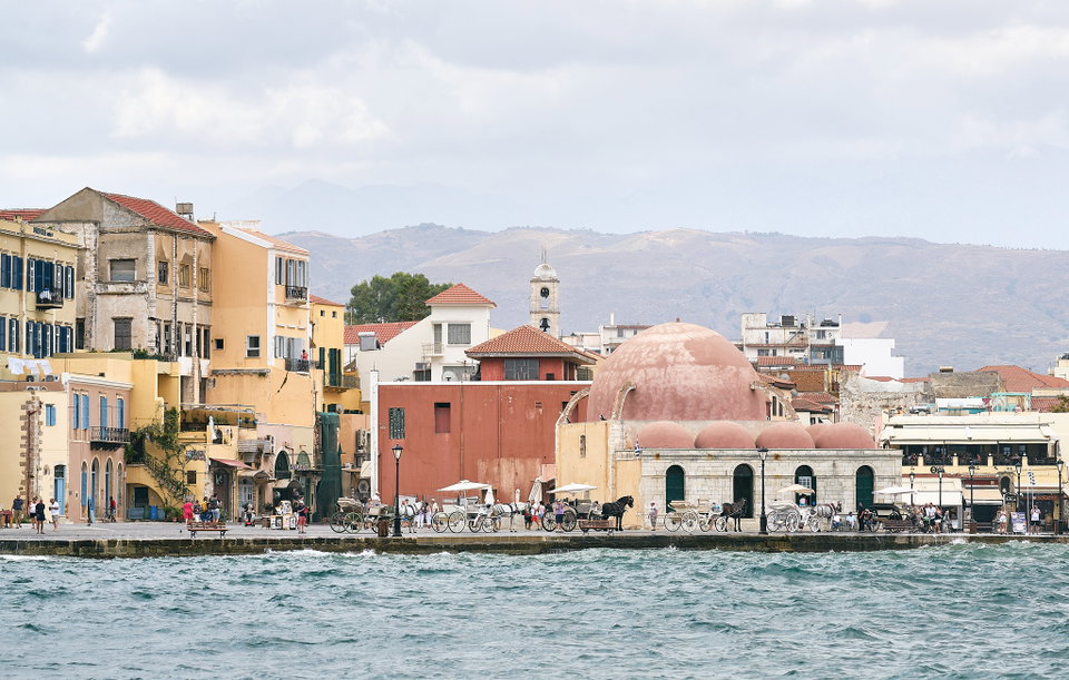 Venetian harbour of Chania at dusk, with the lighthouse and colourful waterfront buildings reflected in the calm sea