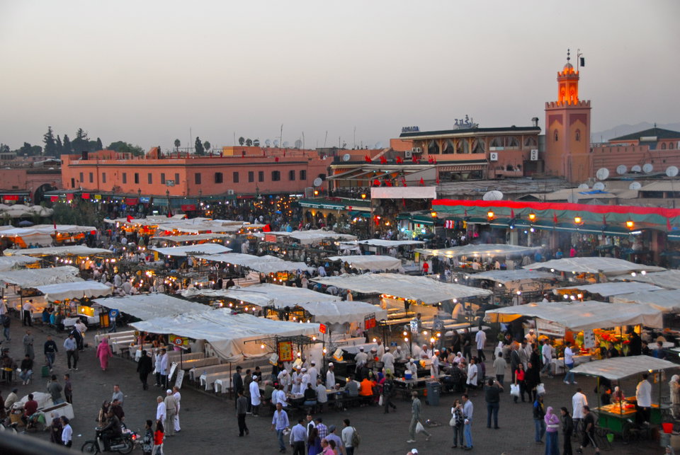 Djemaa el-Fna square at dusk with smoke rising from food stalls and the Koutoubia Mosque minaret in the background