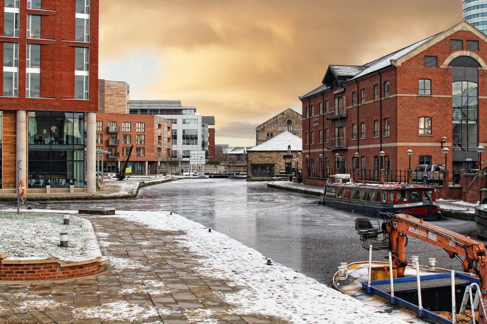 Leeds city skyline reflected in the River Aire at dusk, with Victorian warehouses and modern bridges