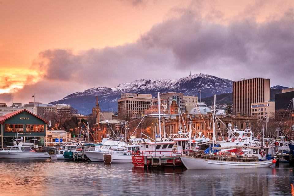 Hobart waterfront at dusk with colourful fishing boats moored at Salamanca Place and Mount Wellington rising behind the city