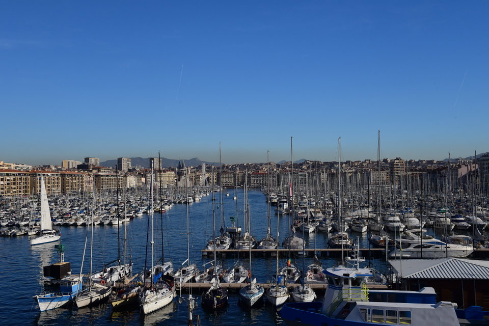 Marseille's Vieux-Port at golden hour, fishing boats moored in the foreground and the Basilique Notre-Dame de la Garde crowning the hilltop beyond