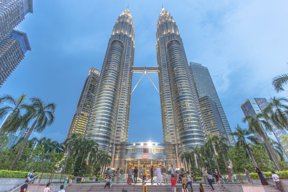 The Petronas Twin Towers rising above the Kuala Lumpur skyline at dusk, surrounded by lush greenery and city lights