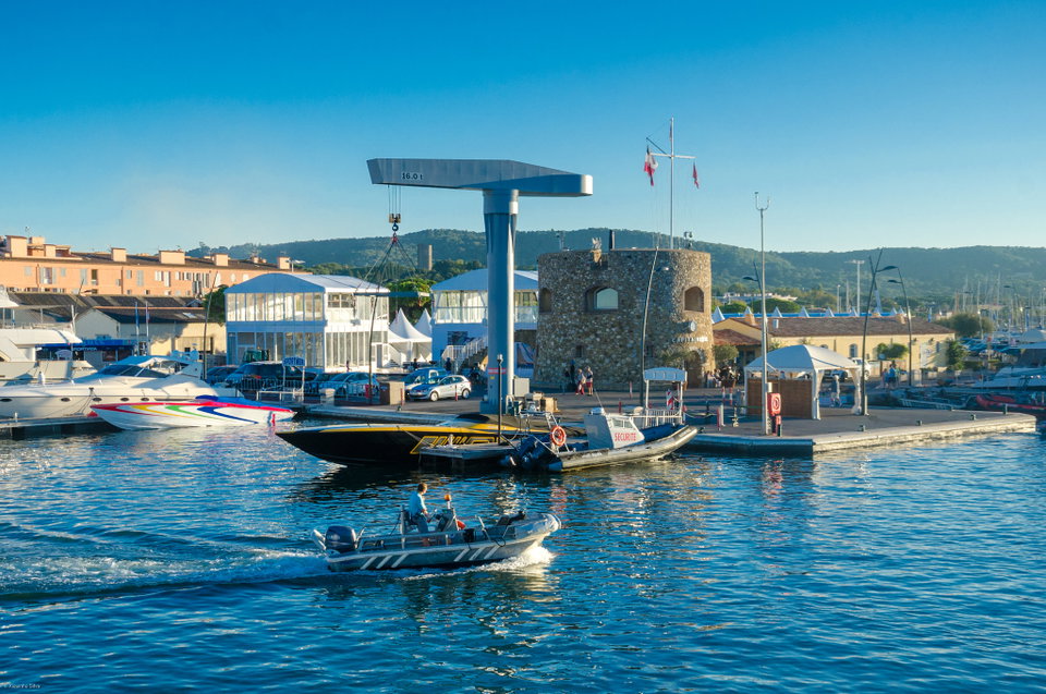 Saint-Tropez harbour at golden hour, yachts moored along the quay with the village's terracotta rooftops rising behind