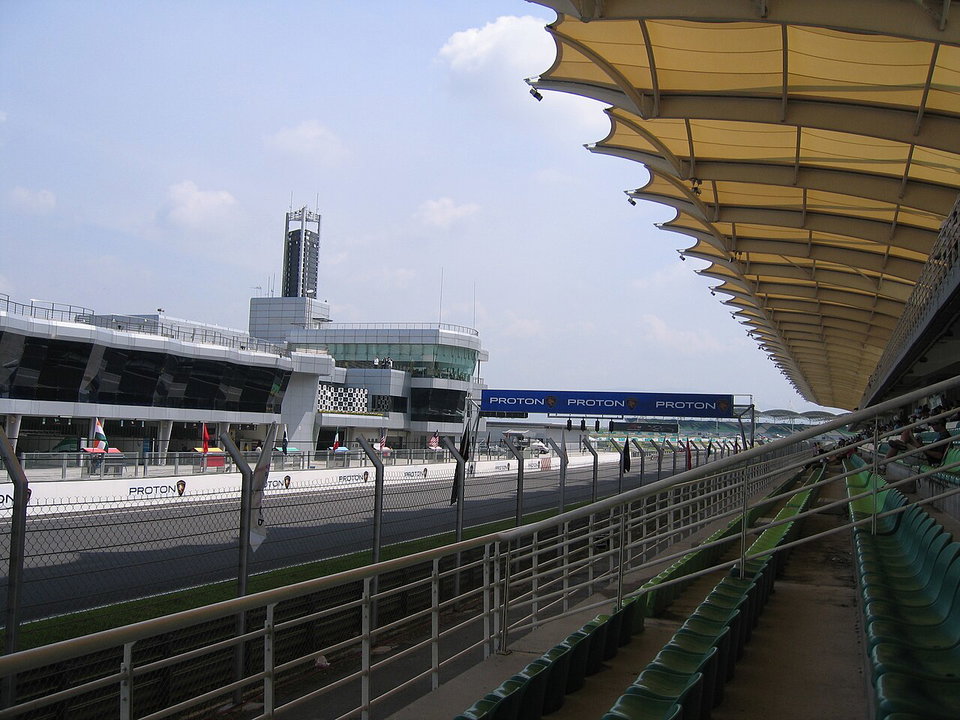 Sepang International Circuit race track under floodlights at dusk, with the Malaysian skyline in the background