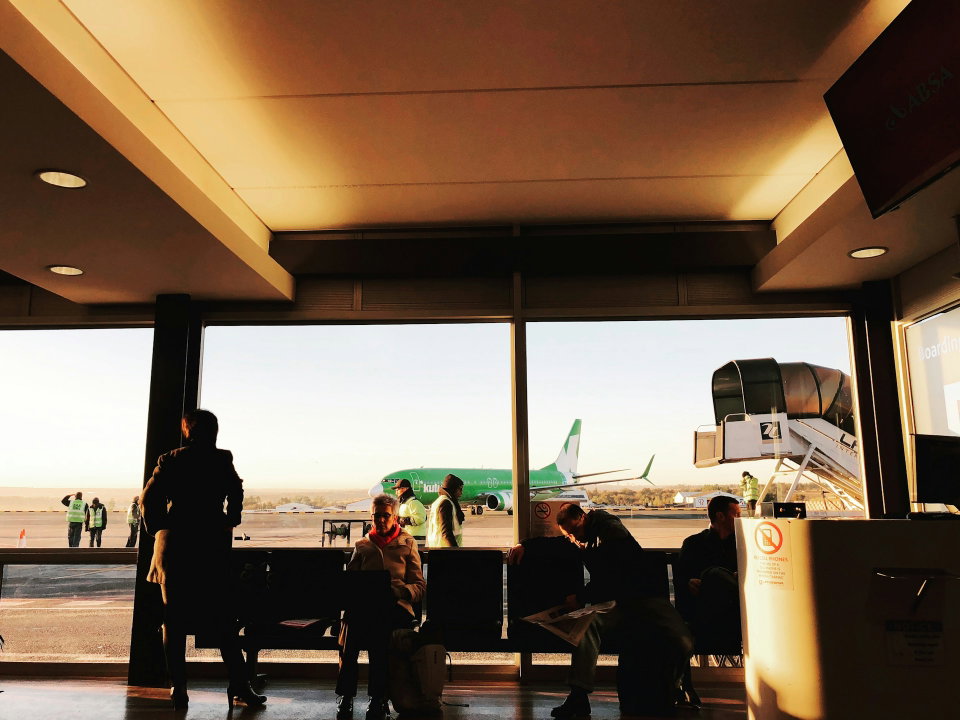 Travellers wait to board a flight at a South African Airport with a Kulula plane in the background. Photo by Etienne Swanepoel. 