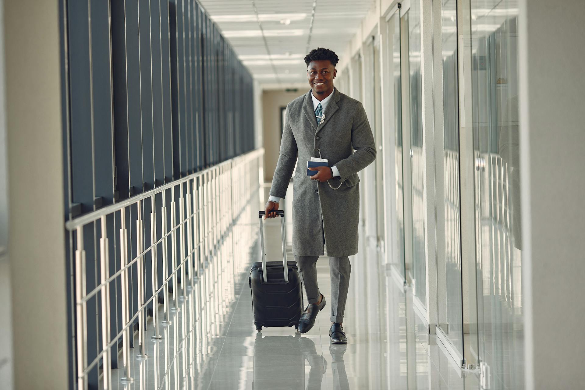 A well dressed and stylish man walks down an airport corridor pulling his carry on suitcase. Photo by Gustavo Fring.