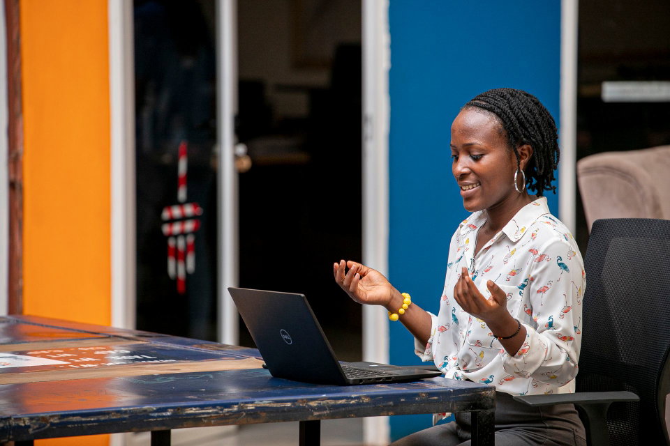 Smiling African woman with dreadlocks having an online video call in a colorful office in Kampala, Uganda. Photo by Eric Okurut