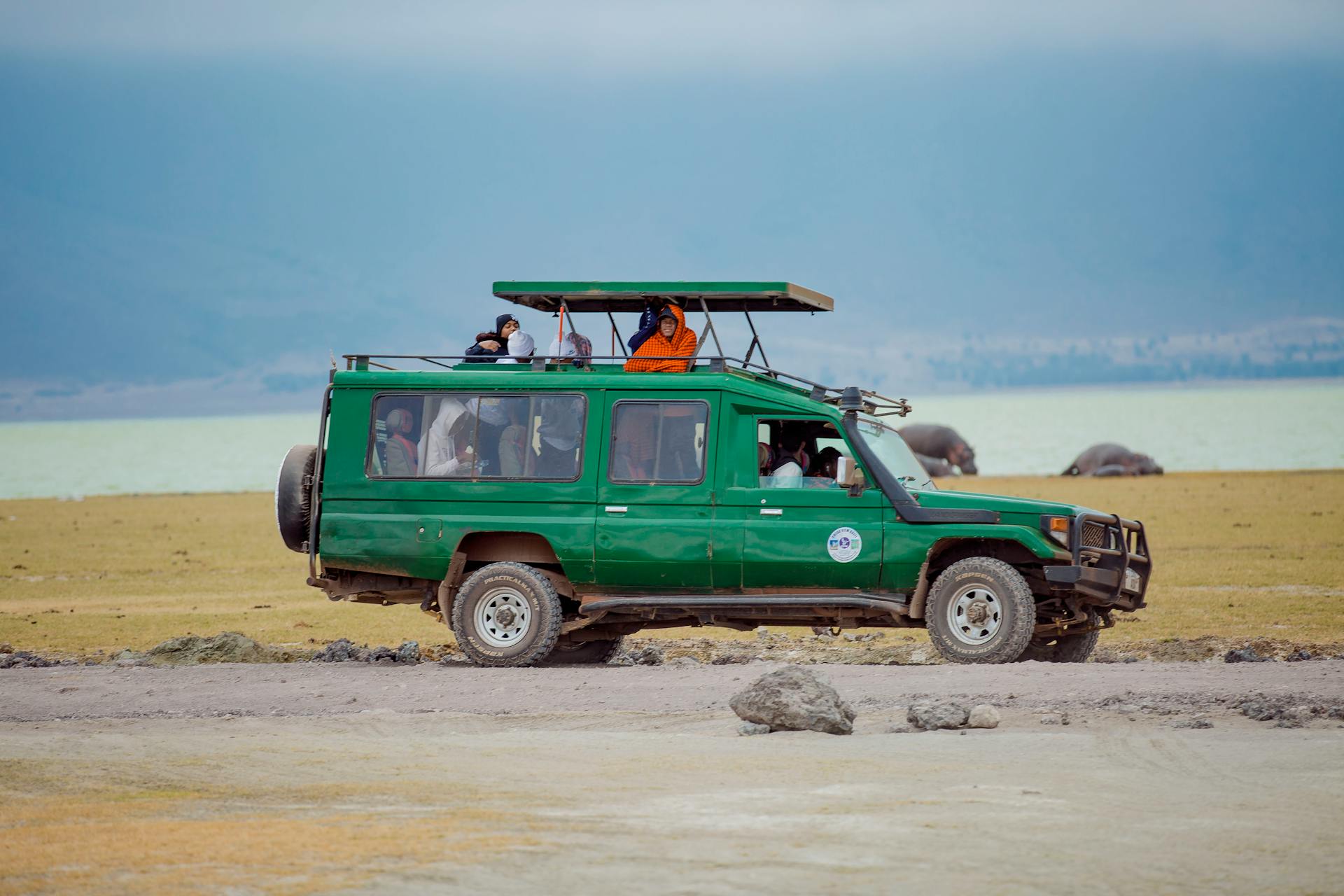 Tourists in a green jeep exploring a national park in Tanzania. Photo by Ramy Photographer.