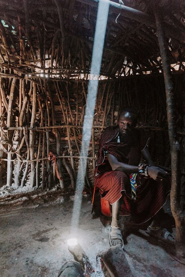 A maasai moran sits inside a village hut. 