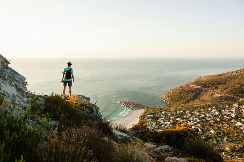 Tourist stands on the edge of a cliff overlooking the ocean. Llandudno, Cape Town, South Africa. Photo by Tim Johnson.